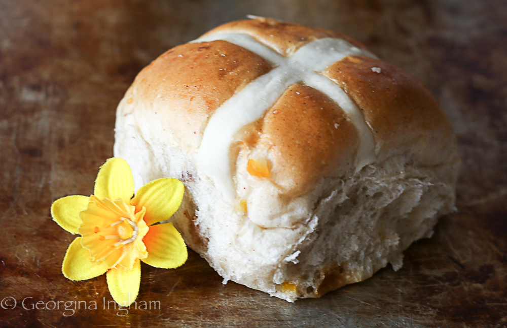 close up of a home baked hot cross bun on rustic wooden board